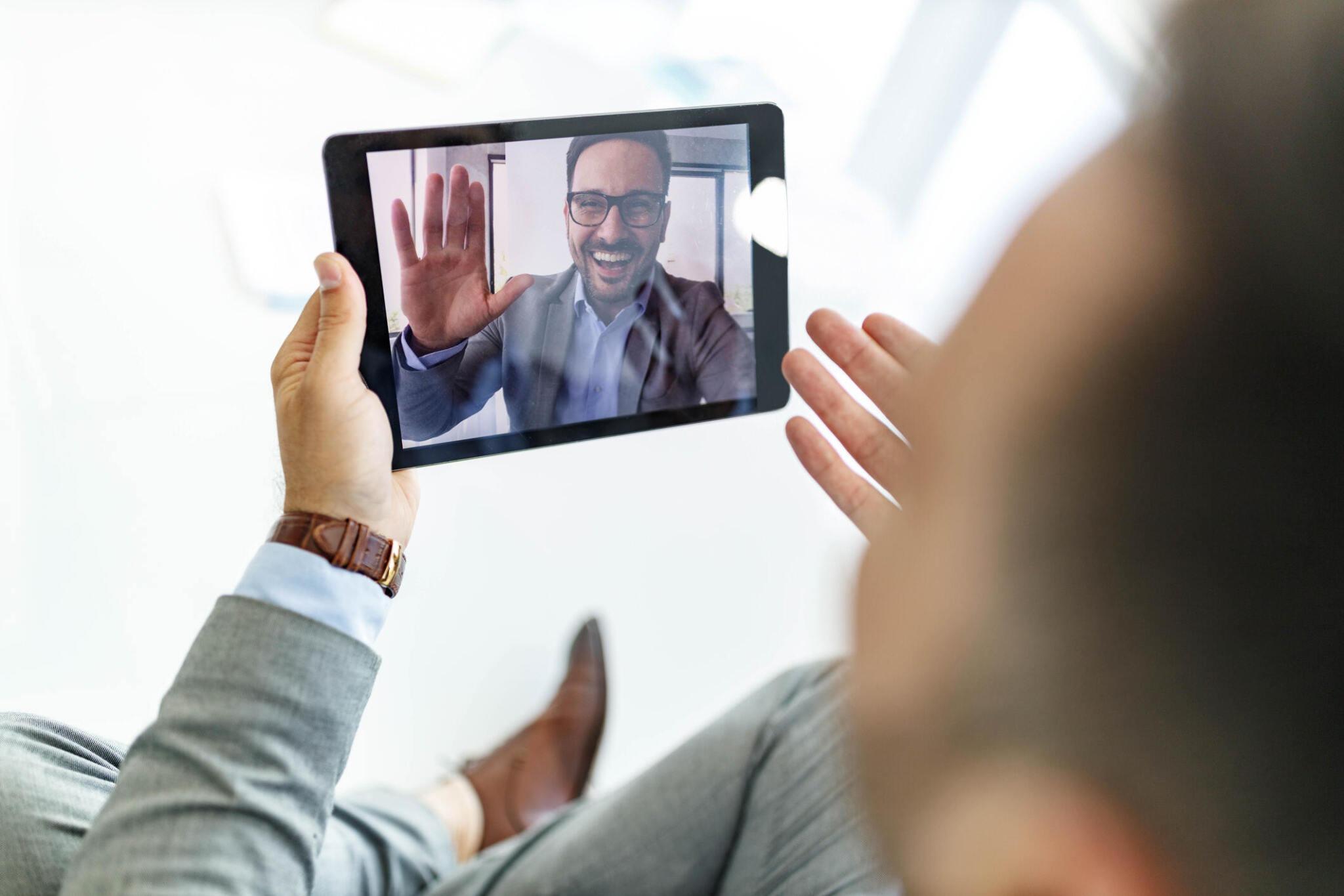 Happy businessman waving while having a meeting with his colleague through a video call over digital tablet