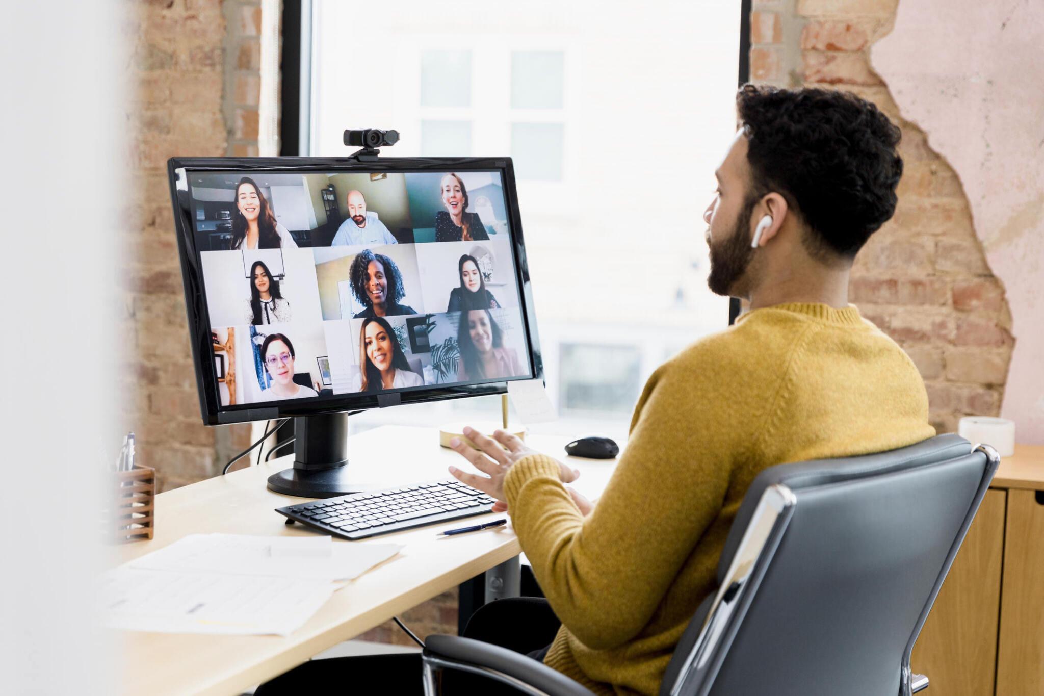 The team lead visits with his team virtually to review feedback from the customer using the desktop computer and apple AirPods