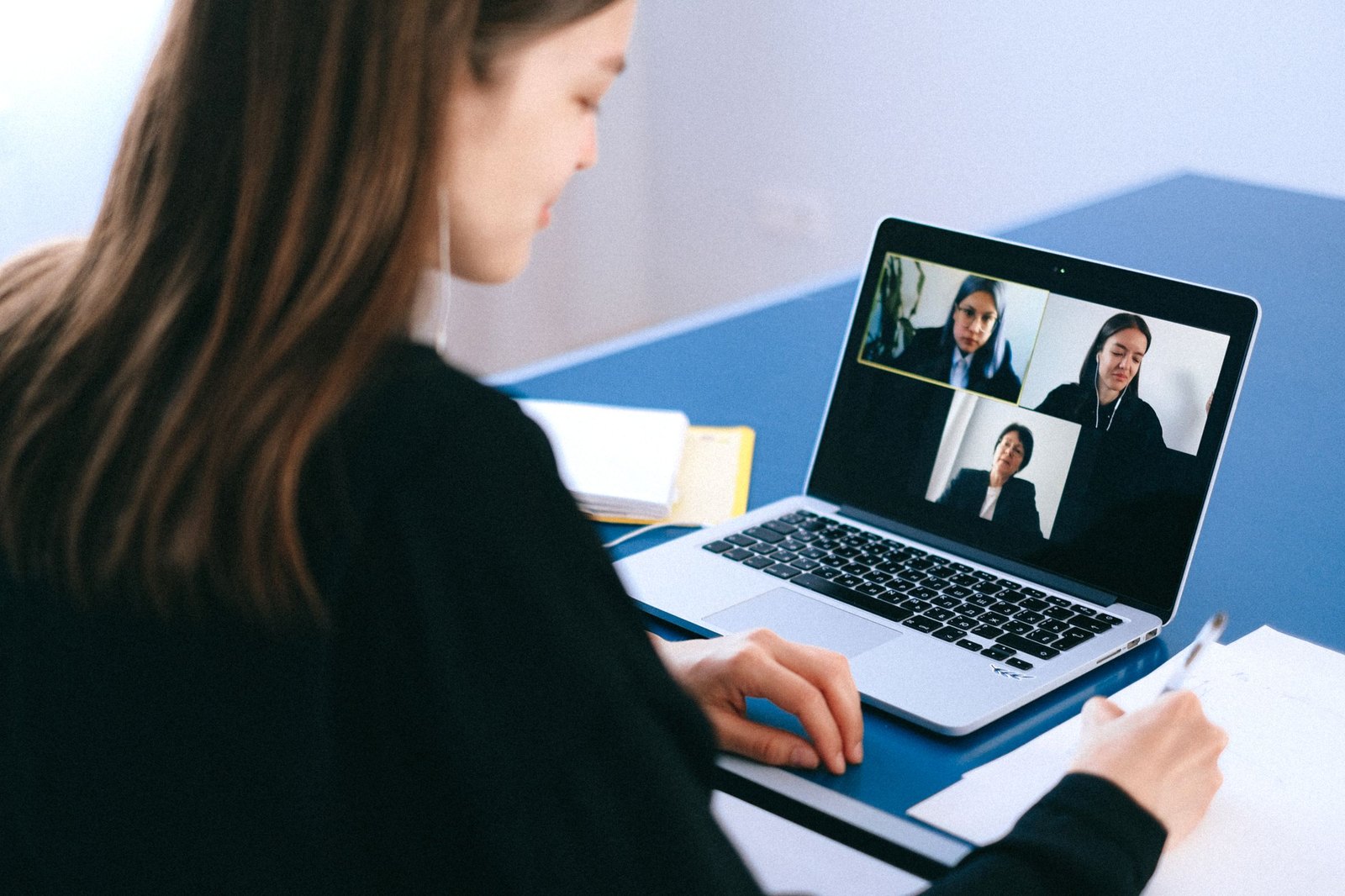 Woman taking notes during a video call with three colleagues on her laptop